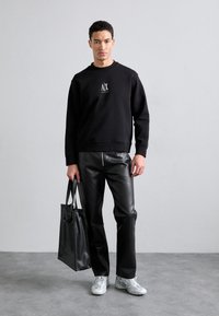 Black sweatshirt with logo, black faux leather pants, and a structured black tote bag. White sneakers with silver accents.