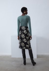Haut mint à manches longues et ajusté, associé à une jupe midi florale noire. Le mannequin porte des bottes noires jusqu'aux genoux. Design simple et élégant.
