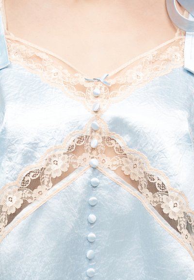 Κοντινή λήψη ρουχισμού από γαλάζιο σατέν με μπεζ δαντέλα λουλουδιών και κουμπιά καλυμμένα κατά μήκος του κέντρου μπροστά.