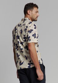 Korte mouw shirt in beige met een donker bloemenpatroon. Voorzien van een standaard kraag, knoopsluiting aan de voorkant en een relaxte pasvorm. Katoenen stof.