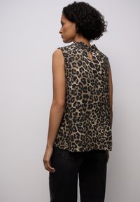 Beżowo-czarna bluzka bez rękawów w gepardzie wzory, z małym detalem w kształcie dziurki z tyłu i luźnym krojem. Materiał wydaje się gładki.