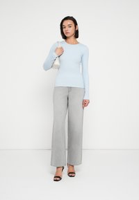 Μπλε ανοιχτό μακρυμάνικο εφαρμοστό τοπ, συνδυασμένο με ψηλόμεσα γκρι τζιν παντελόνια με φαρδιά πόδια και μαύρα σανδάλια με τακούνι. Μικρή λευκή τσάντα προσθέτει έμφαση στην εμφάνιση.