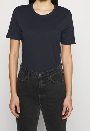 Camiseta de manga corta azul marino con cuello redondo y un sutil detalle de logo en el pecho, combinada con jeans negros de cintura alta.