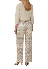 Beige kort jasje met driekwart mouwen, gecombineerd met wijde broek met een zigzagpatroon in neutrale tinten.