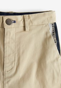 Pantaloni beige in cotone dalla texture liscia, dotati di chiusura con bottone in metallo, tasche laterali e cinturino con motivo a fantasia in blu navy.