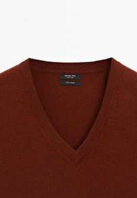 Maglione in cashmere color ruggine con scollo a V, colletto a costine e etichette che mostrano il marchio "Massimo Dutti" e "100% Cashmere". Texture morbida.