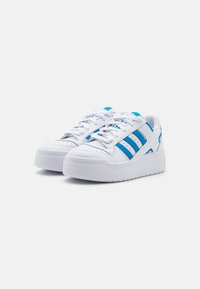 White sneakers with blue accents, featuring three side stripes, textured leather, a thick white sole, and lace-up design.