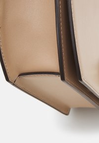 Bolso de mano de cuero beige con textura suave y forma estructurada. Presenta ribetes y costuras de color marrón oscuro. El interior es visible.