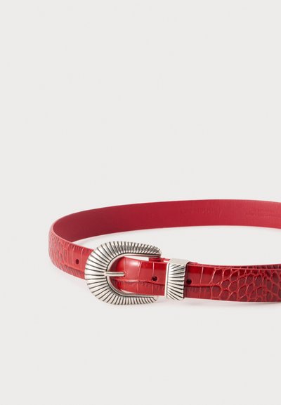 Ceinture rouge en cuir synthétique façon crocodile avec une grande boucle argentée texturée et un passant argenté assorti sur fond blanc.
