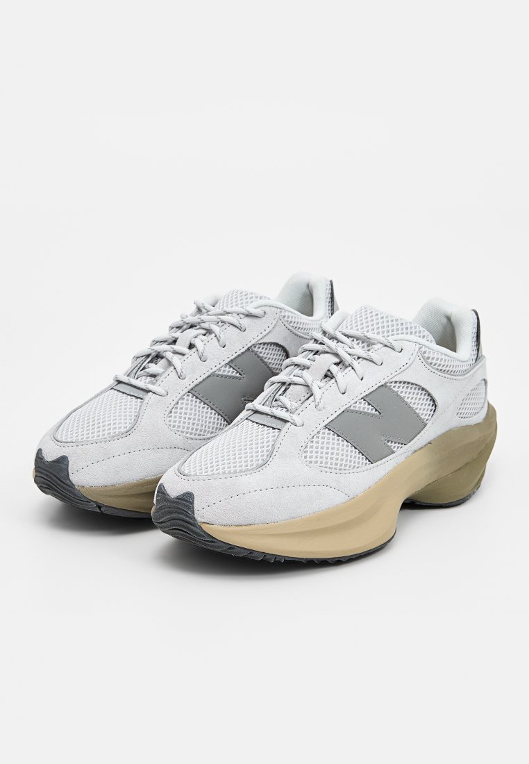 Chaussures de sport avec une tige en mesh et en daim gris clair, accents gris, et une semelle épaisse beige. Dotées d'un système de laçage et d'une surface texturée.