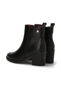 Botas de cuero negro hasta el tobillo con punta redonda, tacón bloque medio, paneles laterales elásticos y pequeño acento dorado en el tacón. Interior forrado en rojo.