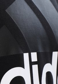 Camiseta atlética negra con tejido texturizado, logo prominente en blanco y diseños geométricos en diferentes tonos de negro.
