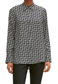 Chemise à manches longues noir et blanc avec col, présentant un motif géométrique et une coupe décontractée. Tissu texturé.