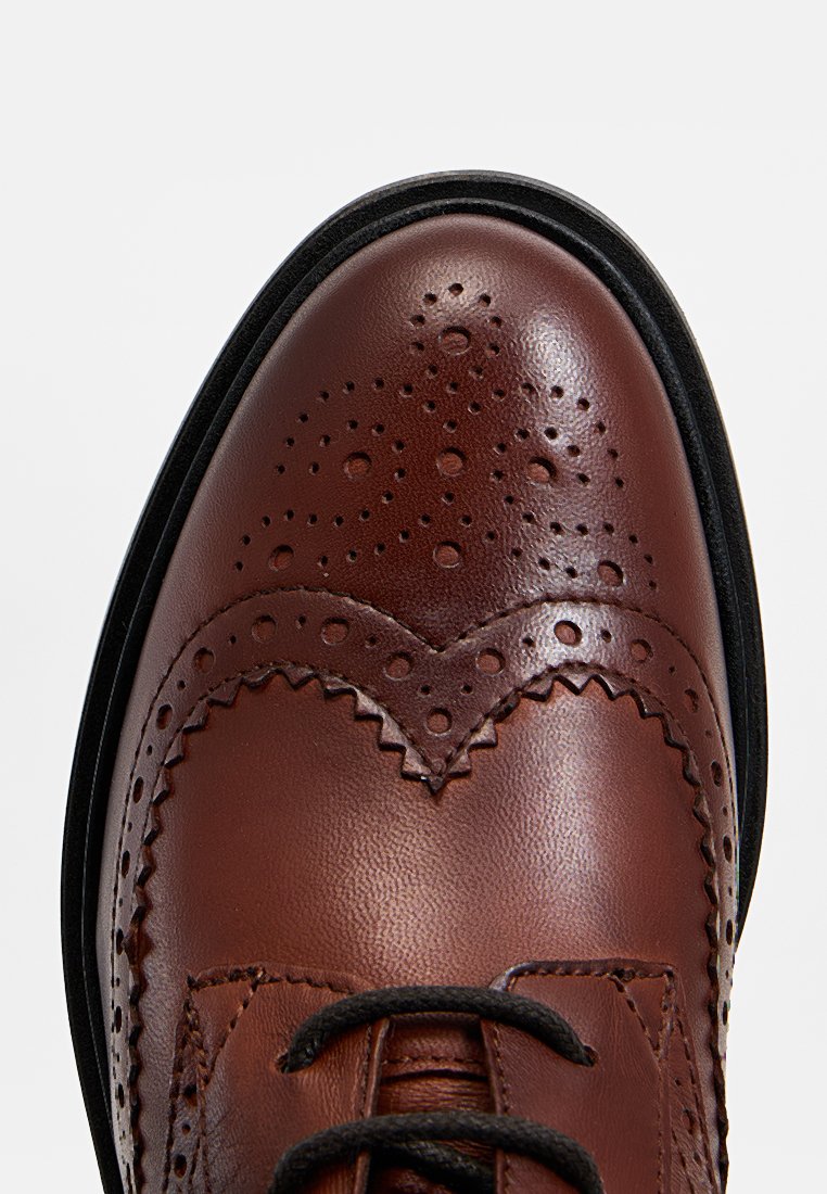 Braune Leder-Brogueschuhe mit kunstvollen Perforationen, strukturiertem Design, runder Zehenform und schwarzer Gummisohle. Die Schnürsenkel sind schwarz.