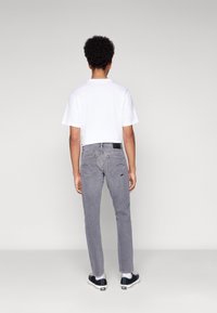 Šedé džíny z denimu a bílé tričko s krátkým rukávem, pohled zezadu. Džíny mají úzký střih a unikátní šití na kapsách.