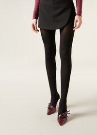 Svarta opaqua strumpbyxor i kombination med en kjol, kompletterat med spetsiga burgundyröda högklackade skor med dekorativa remmar. Mjuk textur och figurnära design.