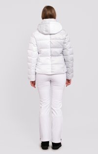 Doudoune en gris clair brillant, avec capuche et coutures horizontales. Associée à un pantalon de ski blanc et des bottes noires, offrant une coupe décontractée.