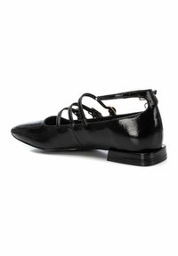 Bailarinas de charol negro con puntas afiladas, correas ajustables en el tobillo y un bajo tacón cuadrado. Superficie lisa con un acabado brillante.