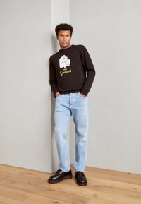 Sudadera negra con un gráfico de dibujos animados y el texto "Los Simpson". Jeans de color azul claro y zapatos de color marrón oscuro completan el conjunto.