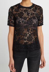 Černý krajkový top s květinovým vzorem, krátkými rukávy, kulatým výstřihem a texturovaným povrchem. Design je poloprůhledný.