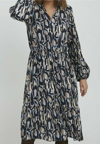 Robe à manches longues dans un motif abstrait bleu marine et beige, présentant un col en V, une taille froncée et une jupe à volants au design fluide.