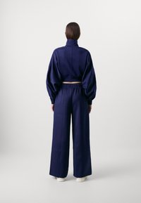 Giacca corta blu navy con colletto alto, abbinata a pantaloni a gamba larga con vita elastica. Tessuto liscio con finitura opaca.