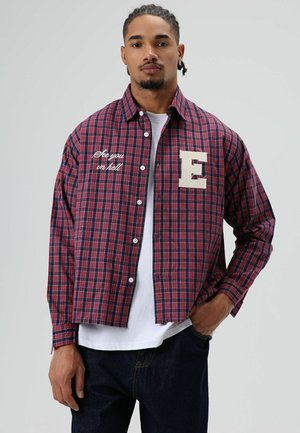 Rood en marineblauw geruit overhemd met lange mouwen, voorzien van een geborduurde "E" en de tekst "See you in hell" aan de voorkant. Witte knopen.