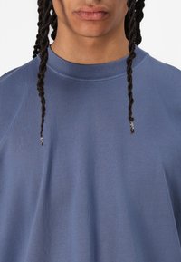 T-shirt de algodão azul com decote redondo, mangas curtas e tecido texturizado. Apresenta detalhes torcidos na parte frontal central.