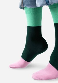 Kolorowe skarpetki z wzorem składającym się z zielonych, ciemnozielonych i różowych sekcji, wykonane z gładkiego, elastycznego materiału.