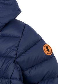 Giubbotto puffer blu navy con texture trapuntata, collo alto e una patch circolare arancione con logo sulla manica.