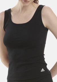 Czarny prążkowany top na ramiączkach z okrągłym dekoltem i grubymi ramiączkami, z małym białym logo Adidasa w dolnym prawym rogu.