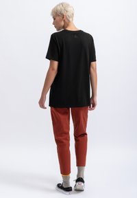 Zwarte katoenen t-shirt met korte mouwen en een afgeronde zoom. Draagt bij rustkleurige broeken en zwarte sneakers, met grijze sokken.