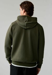 Groene gestructureerde hoodie met een capuchon, voorzien van een diamantpatroon, ribgebreide manchetten en een bandkleurige onderrand. Draagt over een lichtgekleurde shirt.