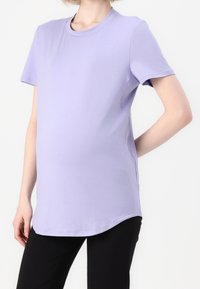 Světle fialové tričko s krátkými rukávy a kulatým výstřihem, vyrobené z hladké látky, má volný střih a zakřivený lem. Kombinováno s černými kalhotami.