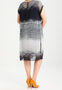 Chiffonklänning i gradient från marinblå till grå. Korta ärmar, nyckelhål i ryggen, sidofickor. Bärs med orange högklackade skor.