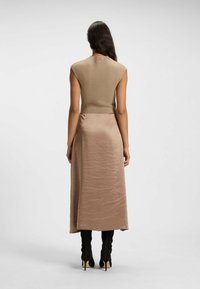 Tan sleeveless top with a fitted design, paired with a long, light brown satin skirt and black knee-high boots. Minimalist aesthetic.