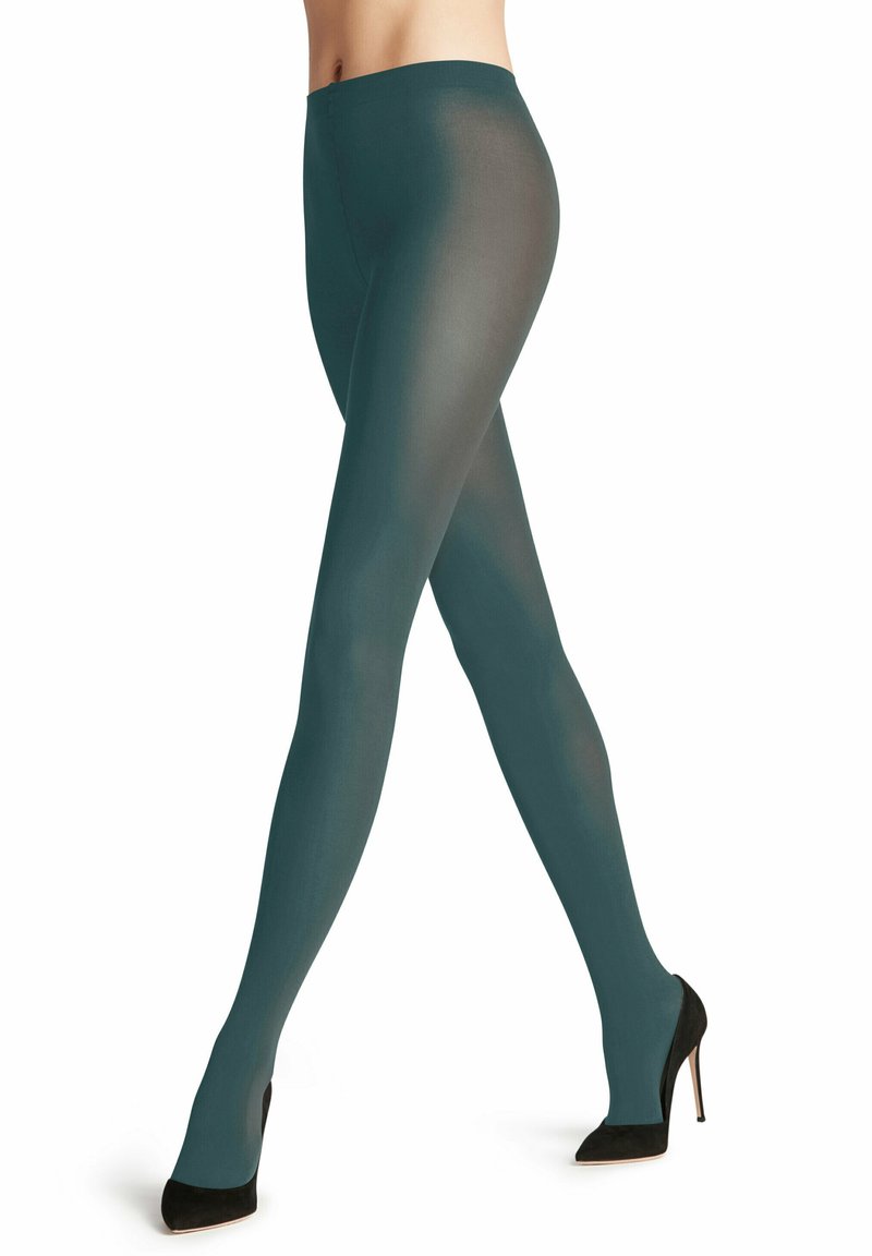 Gambe incrociate con indosso collant opachi color turchese e scarpe con tacco nero, su uno sfondo bianco.