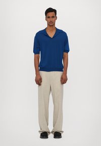 Niebieska koszulka polo z wyciętym kołnierzykiem, krótki rękaw; w zestawieniu z beżowymi spodniami lnianymi; czarne obuwie dopełnia strój.