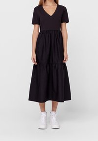 Czarna sukienka z dekoltem w serek i krótkimi rękawami, z marszczonym pasem i zwiewną spódnicą. Noszona z białymi trampkami za kostkę.