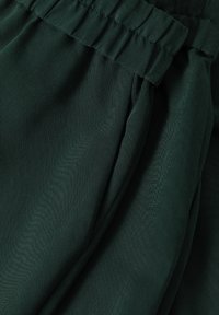 Groene stof met een gladde textuur; heeft een ingezette elastische tailleband en zachte plooien, wat duidt op een ontspannen pasvormontwerp.