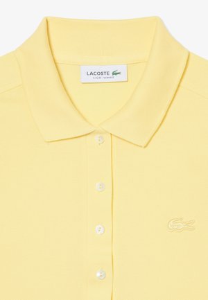Polo Lacoste gialla slim fit con collo, quattro bottoni e logo coccodrillo ricamato sul petto a sinistra.
