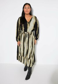 Lange jurk met een V-hals en strikdetail op de taille. Heeft een zwart en beige tie-dye patroon. Gemaakt van een soepele stof met lange mouwen.