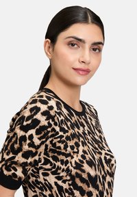Beżowy i czarny sweter w zwierzęcy wzór. Posiada okrągły dekolt i krótkie rękawy, wykonany z teksturowanej, przytulnej tkaniny.
