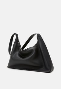 Svart läderhandväska med mjuk, texturerad yta, asymmetrisk design och en enkel axelrem. Har ett blixtlåsfäste upptill.