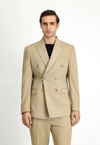 Blazer beige doppiopetto con revers, dettagli in bottone dorato e una tasca sul petto. Tessuto morbido e vestibilità sartoriale.