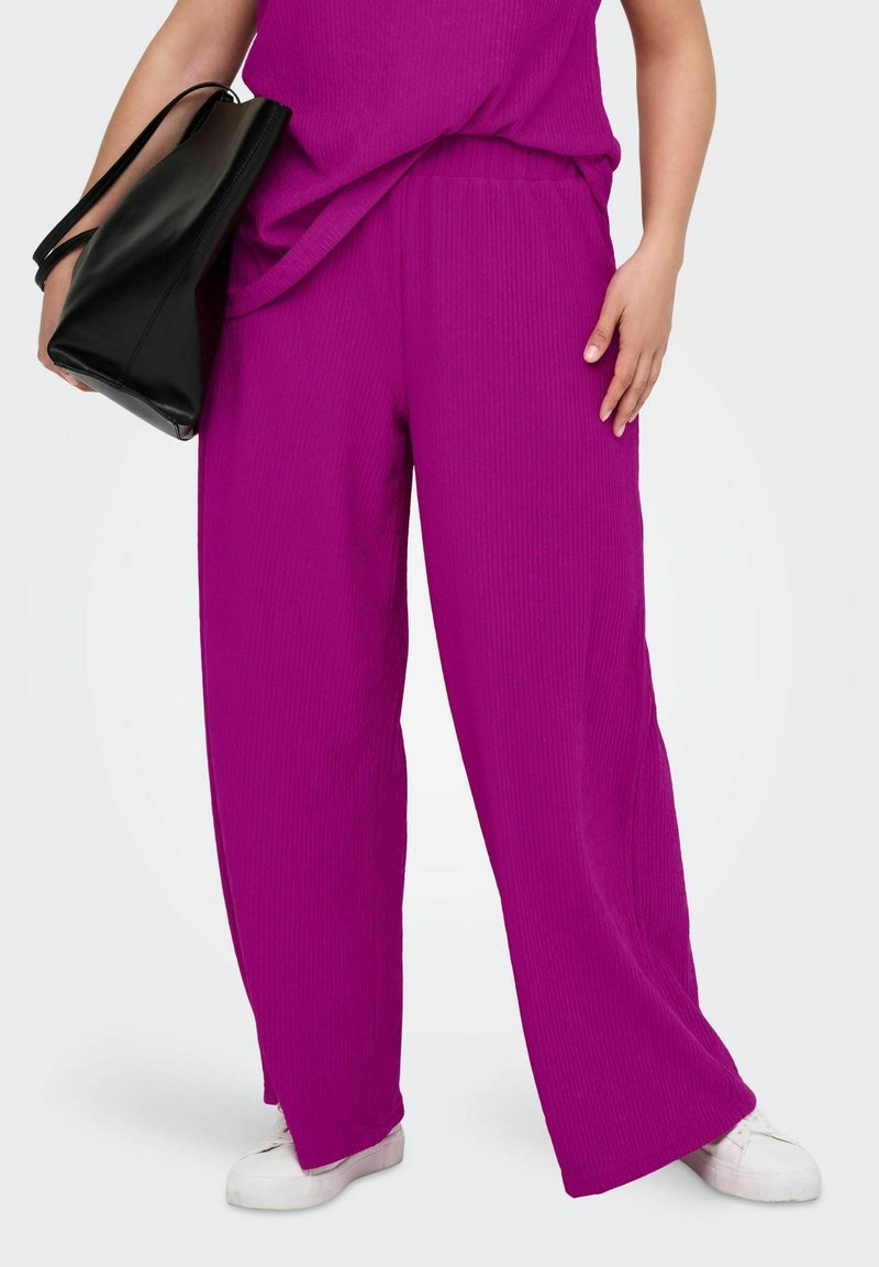 Pantalons larges fuchsia en tissu côtelé avec une taille élastique. Assortis à un sac en cuir noir et des baskets blanches.