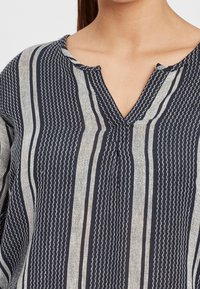 Bluzka w granatowo-kremowe paski z dekoltem w serek, z teksturowanej tkaniny i dekoracyjnym przeszyciem wzdłuż pasków.