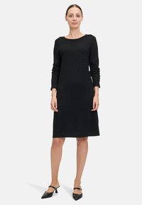 Abito di maglia nera con maniche lunghe, scollo rotondo e dettagli adornati. Tessuto liscio con una vestibilità comoda, che arriva a metà polpaccio.