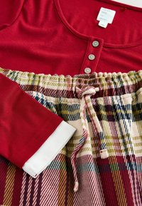 Red long-sleeve top with three buttons at the neckline, paired with elastic-waist plaid pants in red, green, and cream tones, textured fabric.