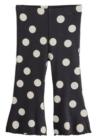 Pantaloni neri a coste svasati con grandi pois bianchi. L'orlo presenta un bordo ondulato che valorizza il design complessivo.